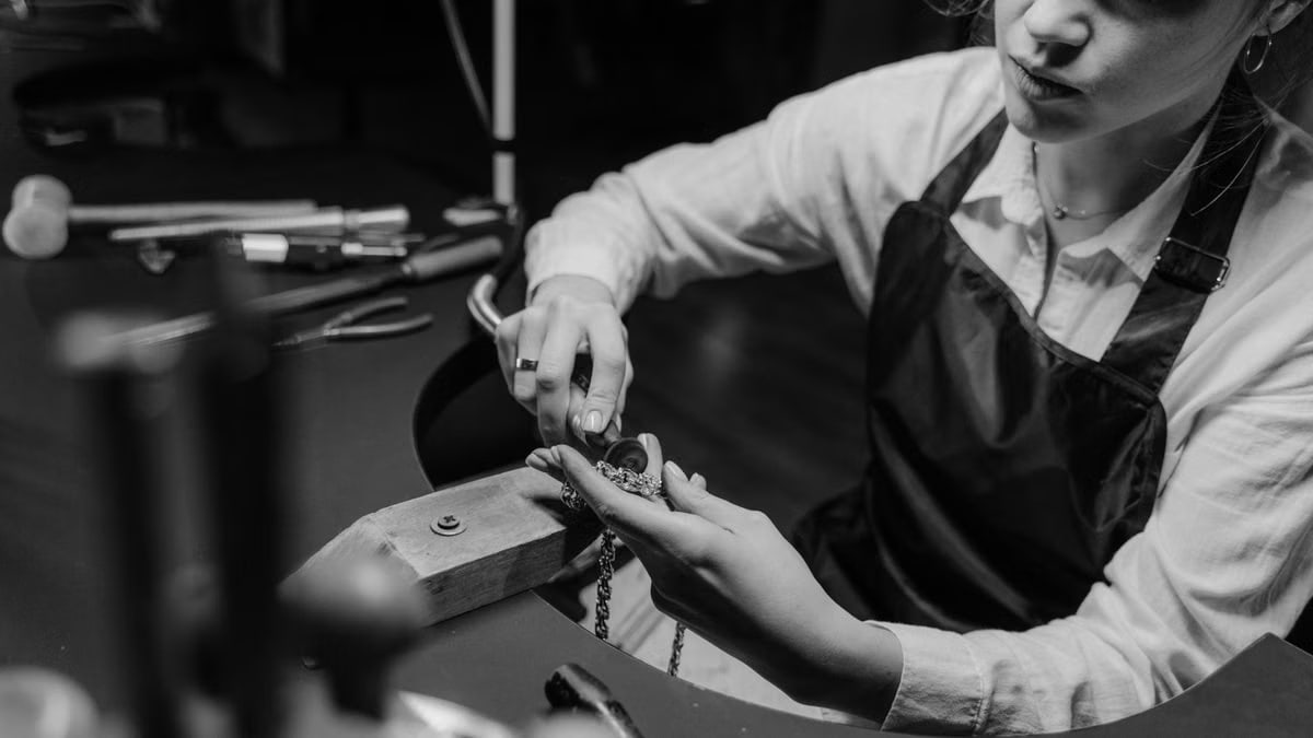 A jeweler meticulously working on a necklace with precision tools in a workshop setting.
